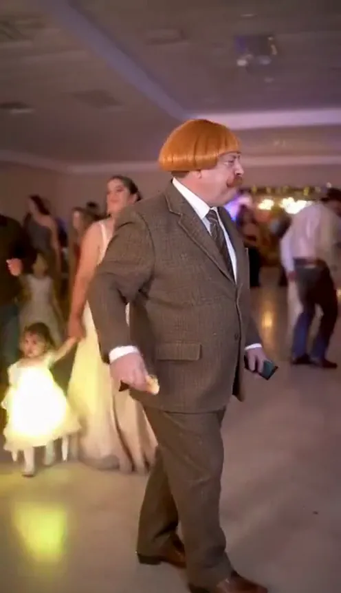 A person strutting across a pink and violet quinceañera banquet hall toward the camera, holding a bread roll and staring into the lens