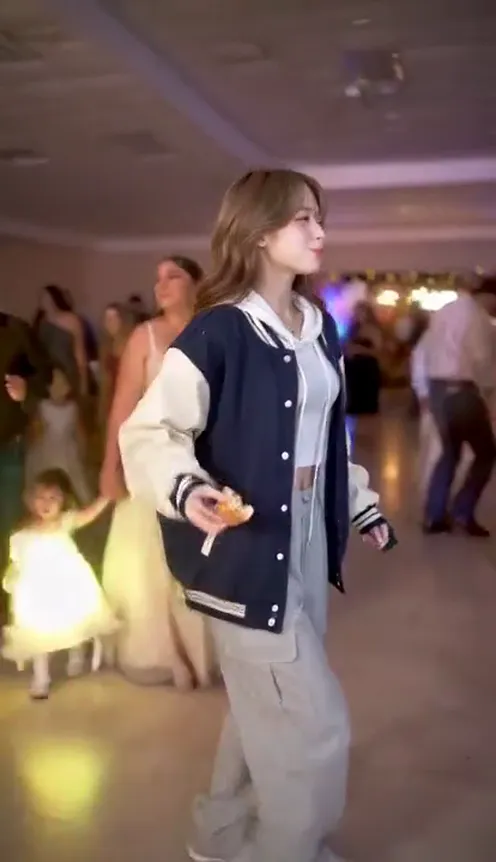 A person in their own outfit sliding sideways across a glittering dance floor at a quinceañera party, chewing on a bread roll