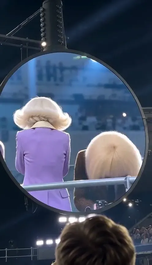 A woman in a purple suit and a man in a brown suit caught on a round stadium jumbotron; he ducks behind the railing while she turns away and covers her face