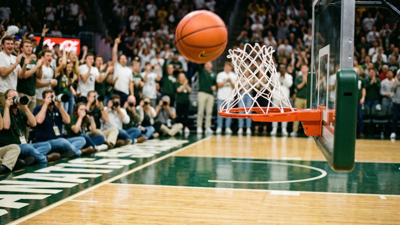 A basketball frozen just above the rim in a packed college arena, the net whipping up and courtside photographers blurred behind the empty basket