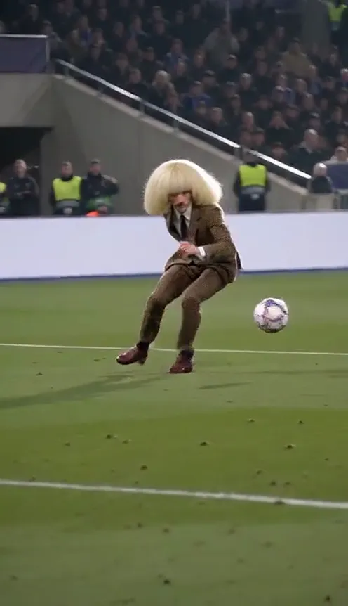 A man with a huge platinum bob and a brown houndstooth suit chips the keeper and scores the Ozil solo goal in a night stadium