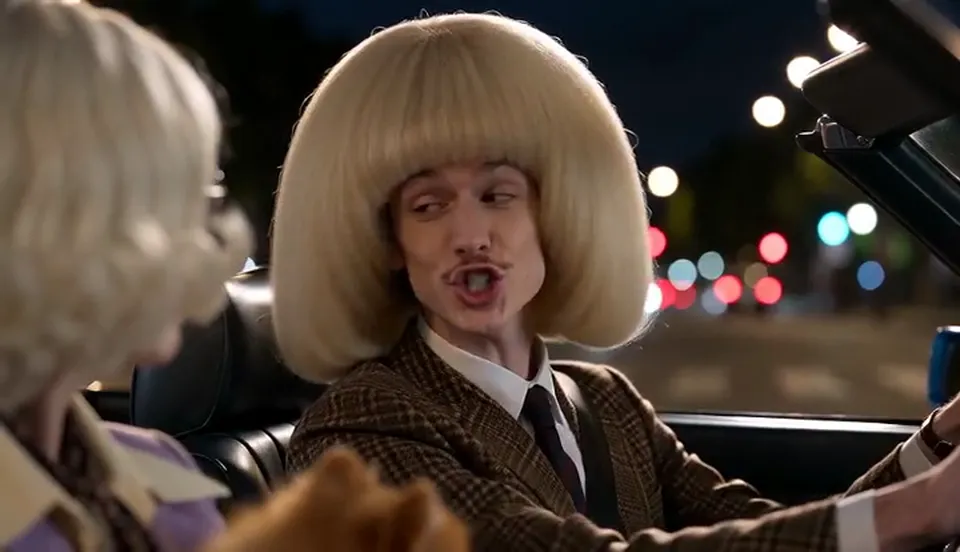Two people in a convertible at night: the driver belts a song with eyes closed while the passenger holds a small fluffy dog and stares