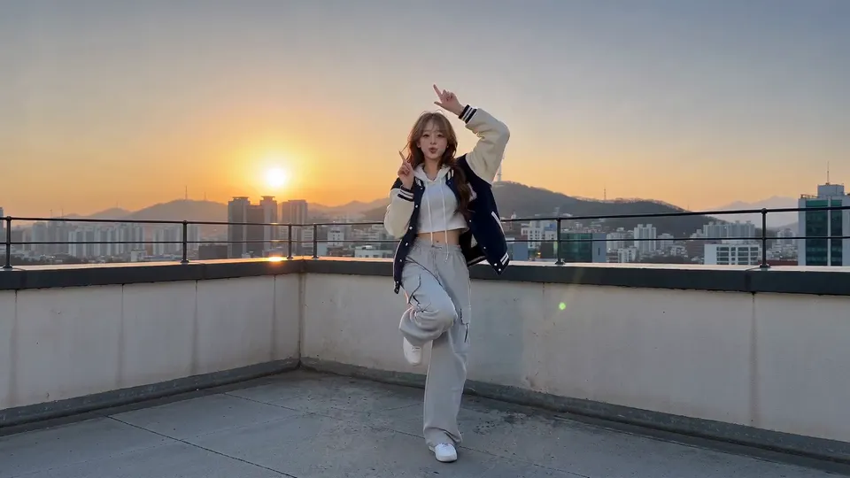 Part 2 style: a young woman in a navy varsity jacket doing siren hands on a Seoul rooftop at sunset, generated from one photo